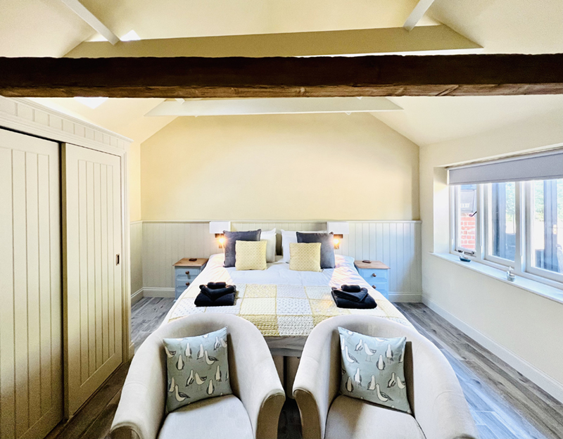 Beautifully decorated cottage bedroom with double bed, tub chairs, large double wardrobe and exposed beam